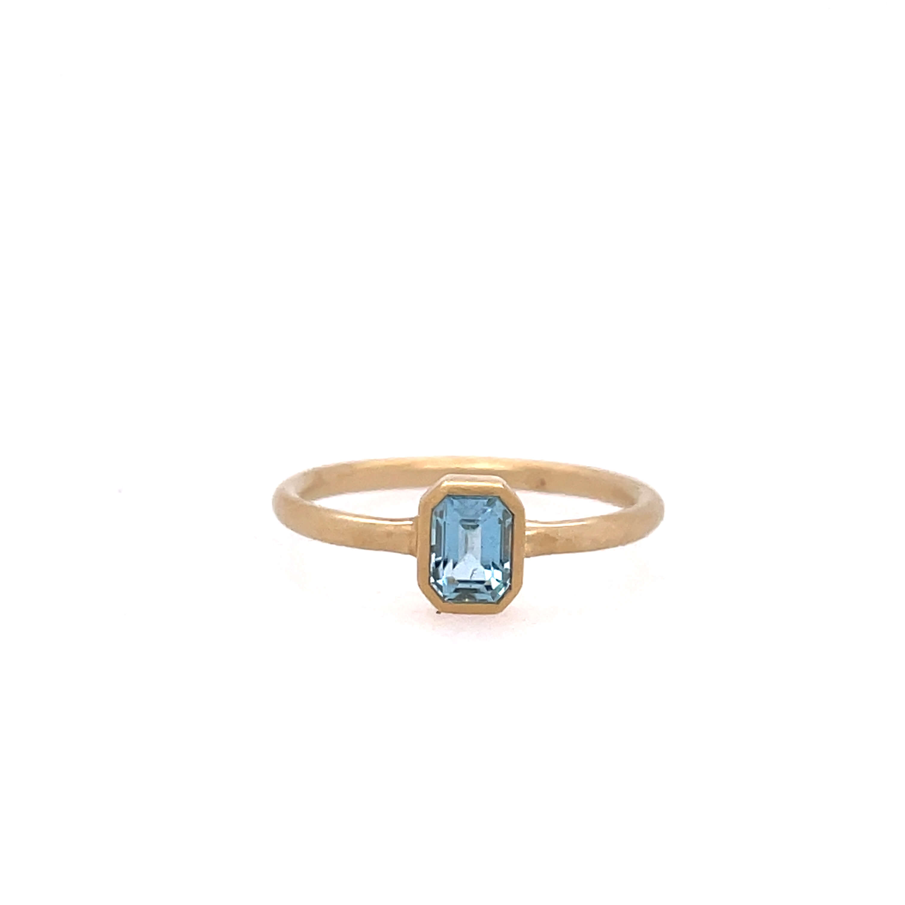 One yellow gold ring with a plain band and a bezel set emerald cut gemtone in the center, set against a white background.