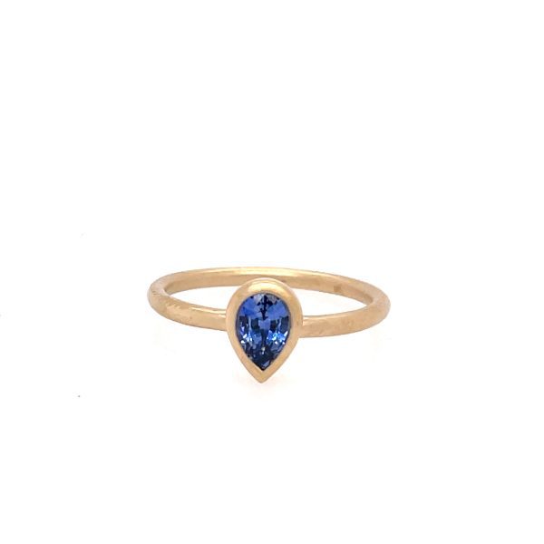 One yellow gold ring with a plain band and a bezel set pear shaped sapphire gemtone in the center, set against a white background.