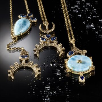 Gold necklaces with sapphire and aquamarine gemstone resting on a moist black surfaced.