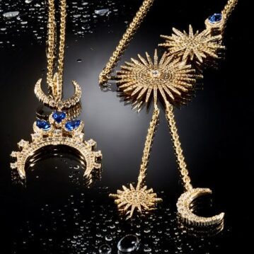 Gold necklaces with sapphire gemstone resting on a moist black surfaced.