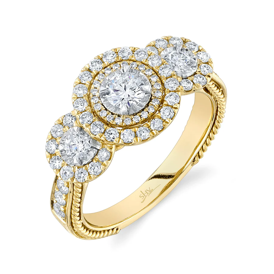One yellow gold ring featuring a triple round cut diamond with surrounded by smaller diamonds as a center point of the piece. Also the ring shoulder filled with diamonds, it is on a white background placed slanted from the camera.