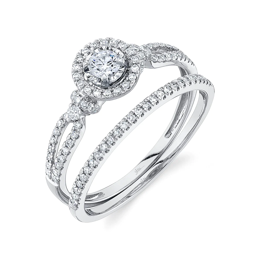 One white gold ring featuring a split shank design filled with diamonds, the ring has mounted diamond as focal point of the piece, it is on a white background placed slanted from the camera.