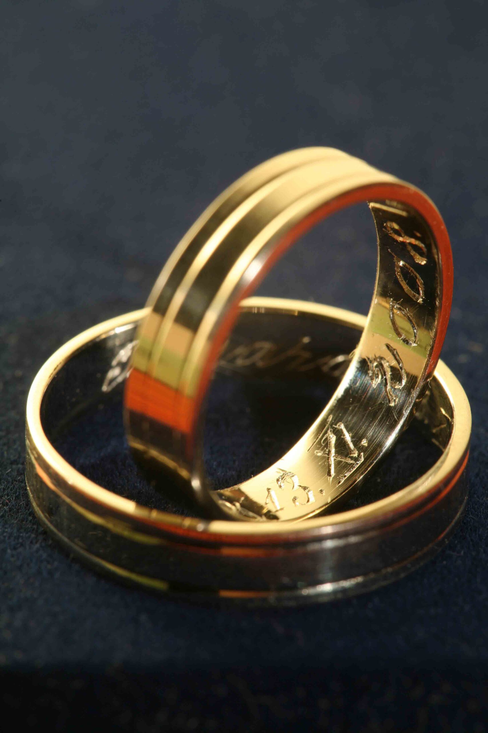 Two yellow gold engraved rings with one ring nestled inside the other, both resting on a black surface.