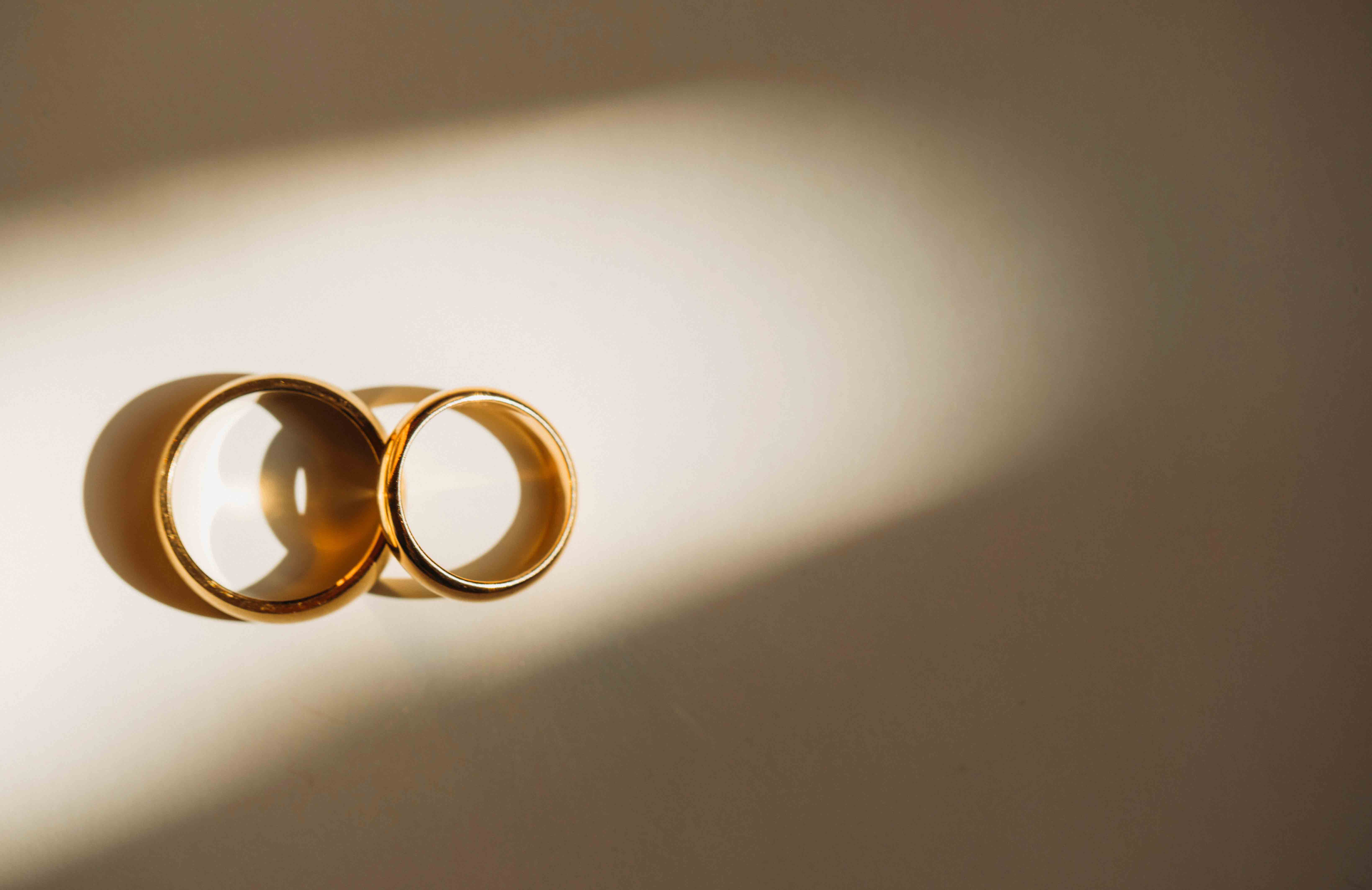 Two yellow gold rings placed one on top of the other on a white background, lit up by a light in the surrounding dark background