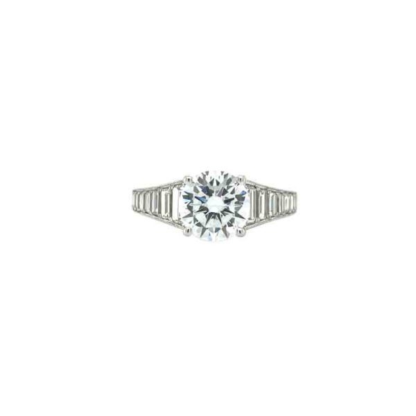 One white gold ring in a prong set round cut diamond as focal point of the piece, featuring a baguette diamonds in the band. The ring sets against a white background.